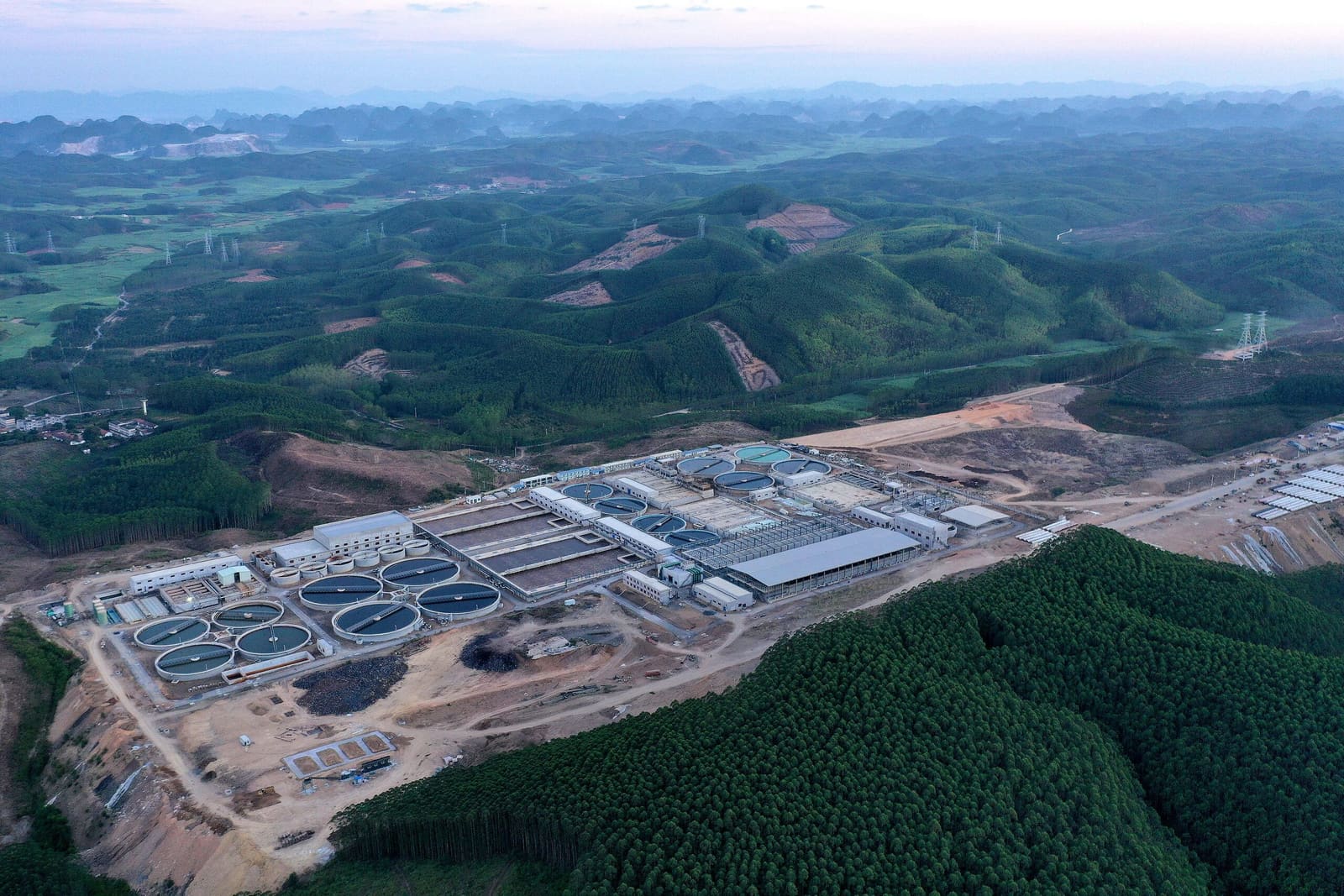An industrial processing complex set against forested hills